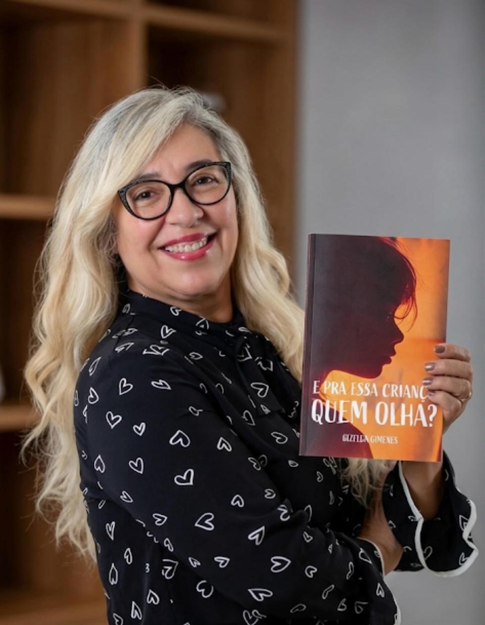 Gizelda Gimenes segurando um exemplar de E pra essa criança, quem olha?